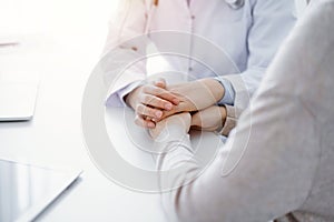 Doctor and patient sitting at the table in clinic office. The focus is on female physician& x27;s hands reassuring woman