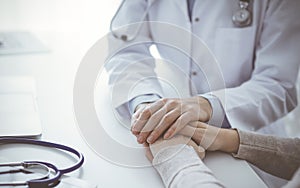 Doctor and patient sitting at the table in clinic office. The focus is on female physician& x27;s hands reassuring woman