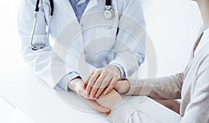 Doctor and patient sitting at the table in clinic office. The focus is on female physician& x27;s hands reassuring woman