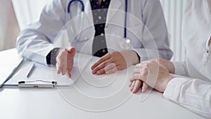 Doctor and patient sitting at the table and talking. The pediatrician in a blue dotted blouse and white medical coat is