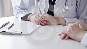 Doctor and patient sitting at the table and talking. The pediatrician in a blue dotted blouse and white medical coat is