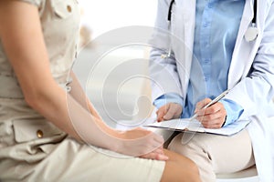 Doctor and patient talking. Physician at work in hospital while writing up medication history records form on clipboard