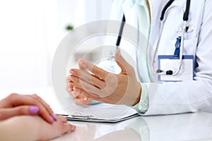 Doctor and patient talking while sitting at the desk in hospital office, close-up of human hands. Medicine and health