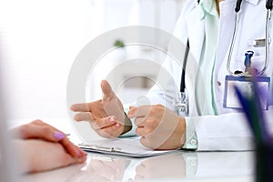 Doctor and patient talking while sitting at the desk in hospital office, close-up of human hands. Medicine and health