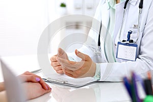 Doctor and patient talking while sitting at the desk in hospital office, close-up of human hands. Medicine and health