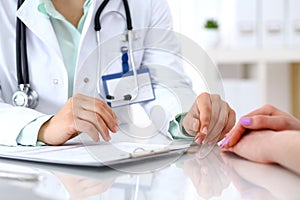 Doctor and patient talking while sitting at the desk in hospital office, close-up of human hands. Medicine and health