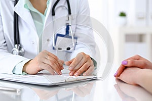 Doctor and patient talking while sitting at the desk in hospital office, closeup of human hands. Medicine and health