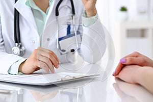 Doctor and patient talking while sitting at the desk in hospital office, closeup of human hands. Medicine and health