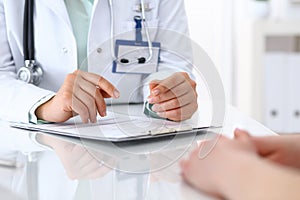 Doctor and patient talking while sitting at the desk in hospital office, closeup of human hands. Medicine and health