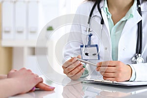 Doctor and patient talking while sitting at the desk in hospital office, closeup of human hands. Medicine and health