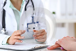 Doctor and patient talking while sitting at the desk in hospital office, closeup of human hands. Medicine and health