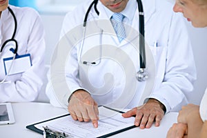 Doctor and patient talking while sitting at the desk in office. Physician pointing into medical history form. Medicin