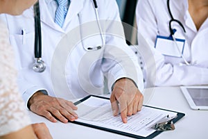 Doctor and patient talking while sitting at the desk in office. Physician pointing into medical history form. Medicin