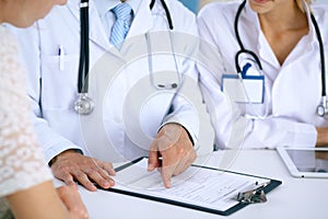 Doctor and patient talking while sitting at the desk in office. Physician pointing into medical history form. Medicin