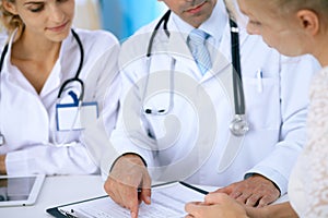 Doctor and patient talking while sitting at the desk in office. Physician pointing into medical history form. Medicin
