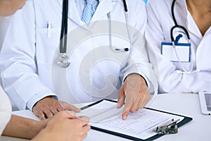 Doctor and patient talking while sitting at the desk in office. Physician pointing into medical history form. Medicin