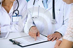 Doctor and patient talking while sitting at the desk in office. Physician pointing into medical history form. Medicin