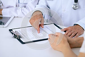 Doctor and patient talking while sitting at the desk in office. Physician pointing into medical history form. Medicin