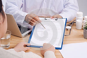 Doctor and patient talking while sitting at the desk in office. Physician pointing into medical history form. Medicine and health