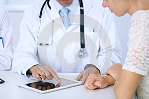 Doctor and patient talking while sitting at the desk in office. Physician pointing into touch pad computer or table