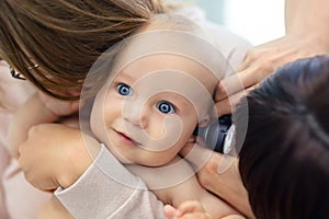 Doctor pediatrist examining childs ear with otoscope. Mom holding baby with hands. Medicine, healthcare ,pediatry and people.