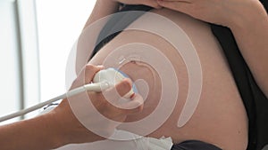 Doctor performing ultrasound sonogram procedure to a pregnant woman. Obstetrician moving transducer on the belly of the