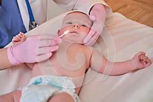 The doctor performs the hygiene of the nose and ears of the newborn baby with a cotton swab. Nurse in uniform rubs the skin of a