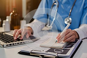 Doctor, physician or practitioner in lab room writing on blank notebook and work on laptop computer.