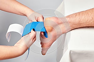 Doctor physiotherapist hands applying kinesiology tape on the ankle of a caucasian man