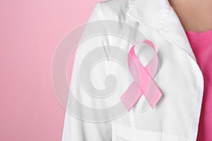 Doctor with pink ribbon on robe against color background, closeup. Breast cancer awareness concept