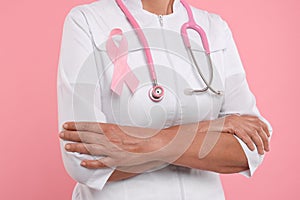 Doctor with pink ribbon and stethoscope on color background, closeup. Breast cancer awareness