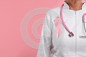 Doctor with pink ribbon and stethoscope on color background, closeup and space for text. Breast cancer awareness