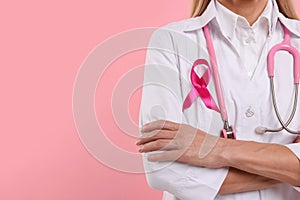 Doctor with pink ribbon and stethoscope on color background, closeup and space for text. Breast cancer awareness