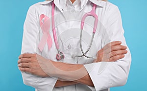 Doctor with pink ribbon and stethoscope on light blue background, closeup. Breast cancer awareness