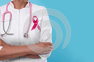 Doctor with pink ribbon and stethoscope on light blue background, closeup and space for text. Breast cancer awareness