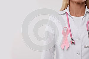 Doctor with pink ribbon and stethoscope on white background, closeup and space for text. Breast cancer awareness