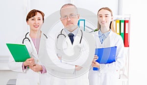 Doctor posing in office with medical staff, he is wearing a stethoscope. Quality medicine concept. Man in white uniform