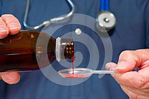 A doctor pours medicine from a bottle into a plastic spoon prior to administering it to a patient.