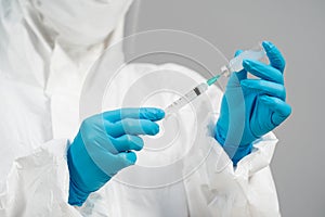 Doctor in PPE suit drawing vaccine bottle into syringe injection medicine