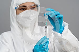 Doctor in PPE suit drawing vaccine bottle into syringe injection medicine