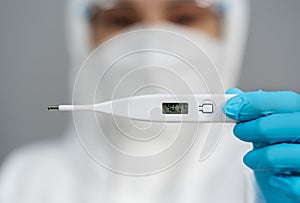 Doctor in PPE suit holding digital thermometer with high temperature
