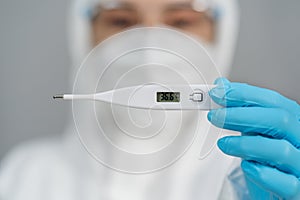 Doctor in PPE suit holding digital thermometer with normal temperature