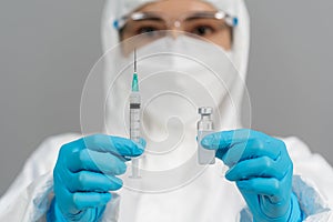 Doctor in PPE suit holding vaccine bottle and syringe injection medicine
