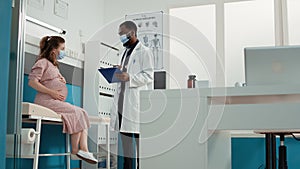 Doctor and pregnant woman with face mask attending checkup visit