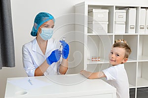 The doctor is preparing to vaccinate the child against the coronavirus. The boy turned around, looked at the camera and smiled.