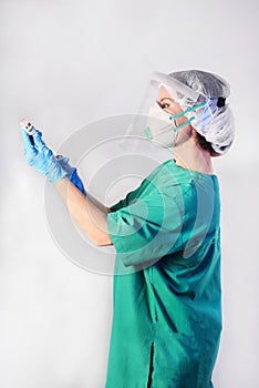 Doctor in protective gear respiratory mask and eye mask in medical latex gloves draws a medicinal fluid into the syringe, half