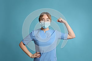 Doctor with protective mask showing muscles on light blue background. Strong immunity concept