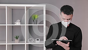 Doctor in a protective medical mask works at a tablet in his office.