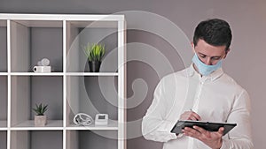 Doctor in a protective medical mask works at a tablet in his office.