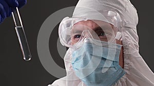 Doctor in a protective medical suit holds an ampoule of coronavirus vaccine in her hands and look into at a test tube. Pandemic an